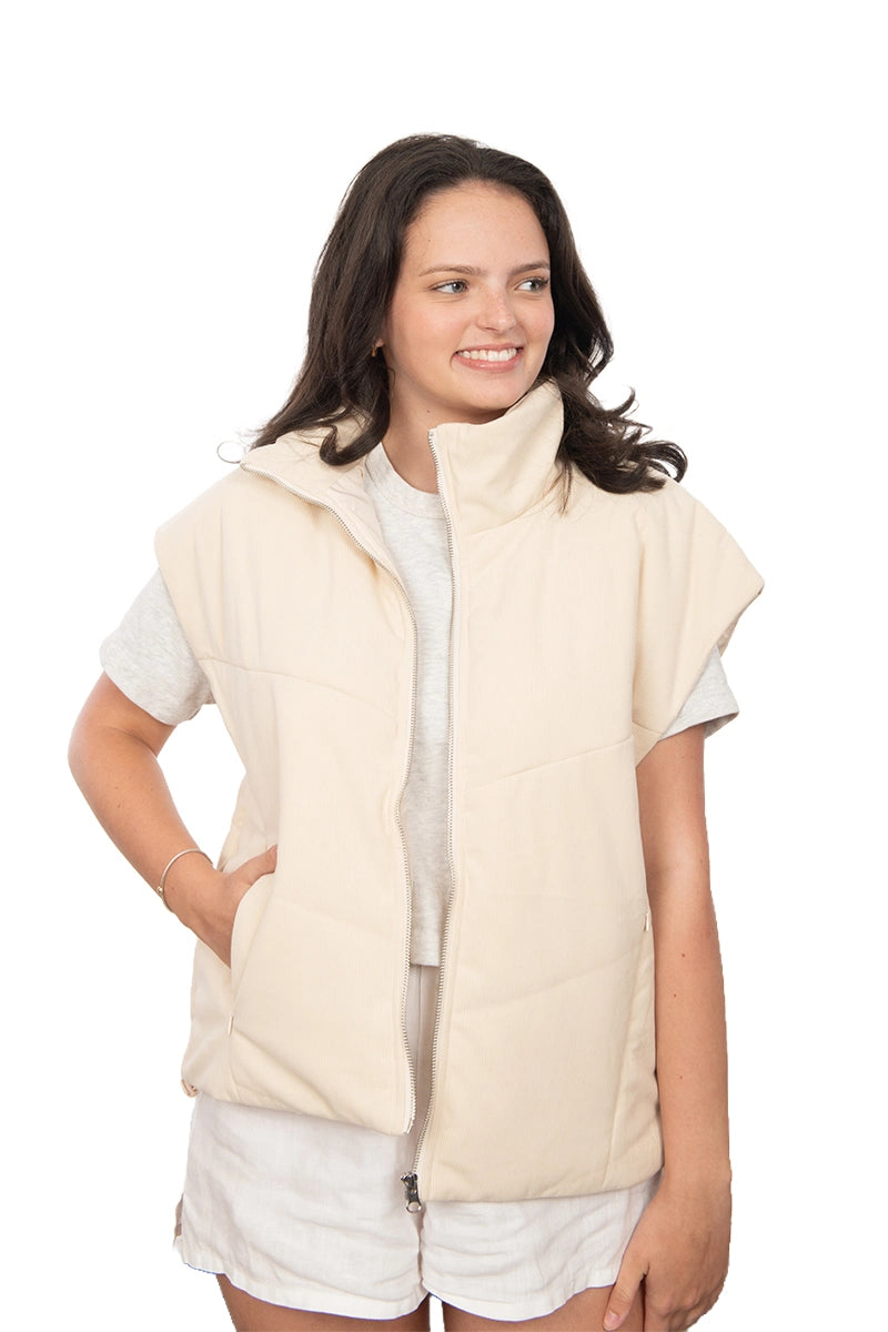 Woman wearing a beige vest over a white shirt and shorts on a white background