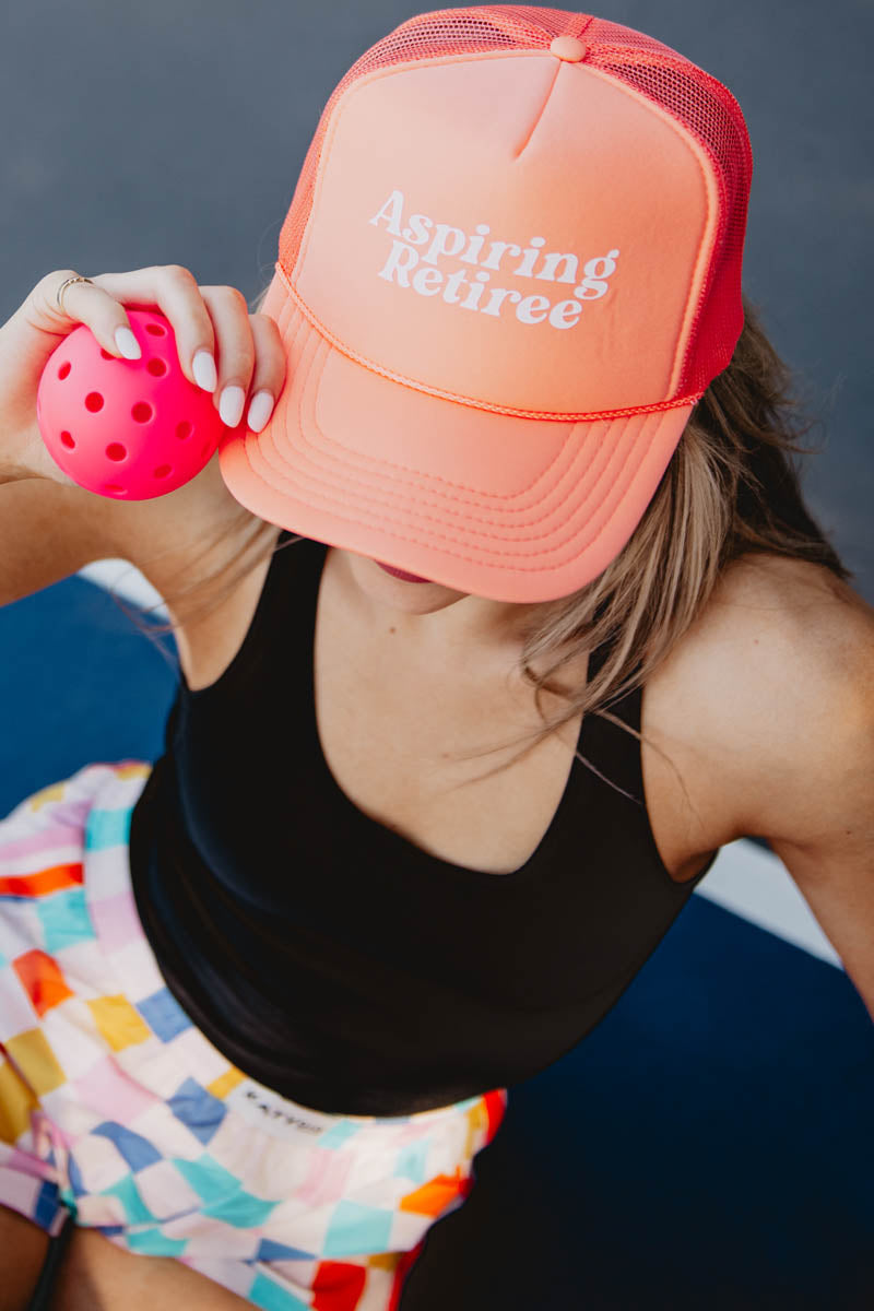 A woman wearing a pink Aspiring Retiree hat and holding a pink pickleball