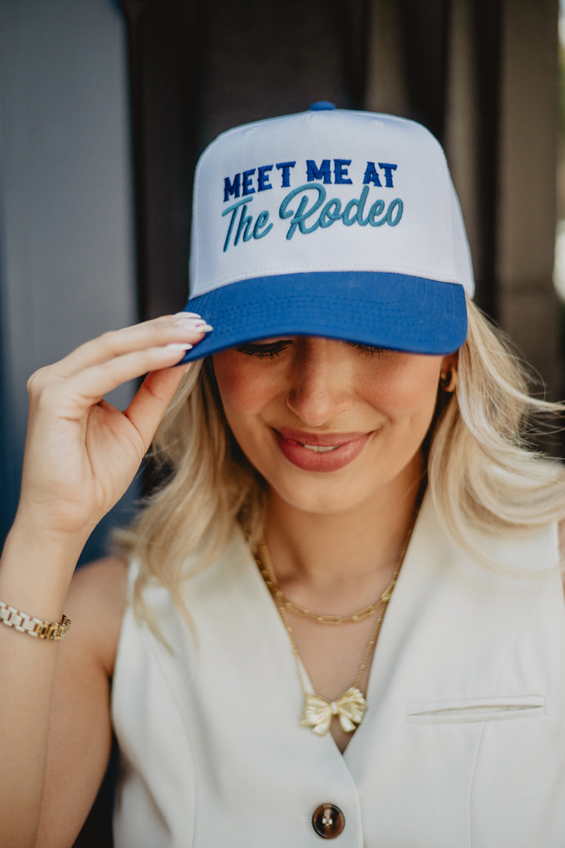 A woman wearing a two toned blue and white trucker hat that says meet me at the rodeo