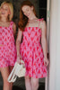 Two women wearing pink dresses with red patterns standing next to each other.